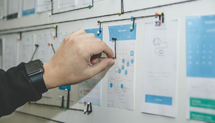 A lot of papers on the wall. A hand is drawing on one paper